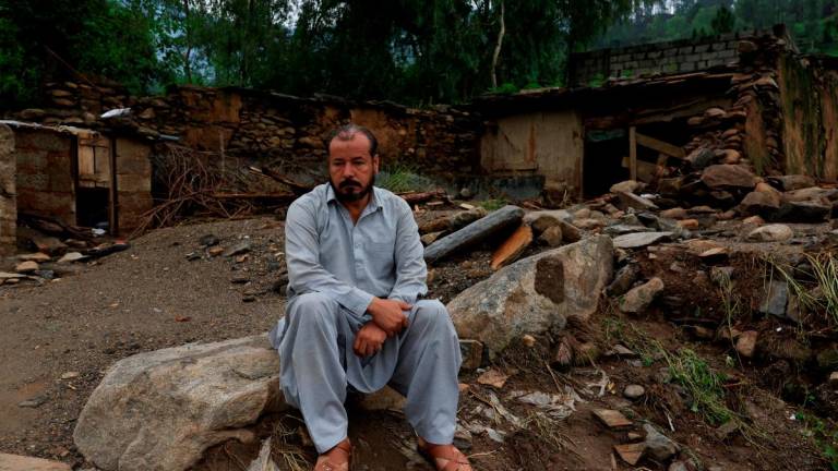 Aziz Ahmed, 45, a school teacher, sits with a damaged house in the background following a storm that caused heavy rains and flooding, in Bayshonai Kalay, Buner district, Khyber Pakhtunkhwa province, Pakistan, August 17, 2025. REUTERS/Akhtar Soomro