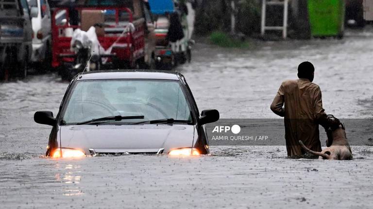 A man along with his dog while a car wade through a flooded street during heavy monsoon rains in Rawalpindi on July 17, 2025. - Aamir QURESHI / AFP