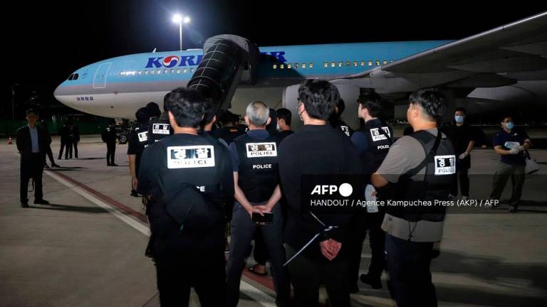 This handout from Agence Kampuchea Press (AKP) taken and released on October 18, 2025 shows South Korean police keeping watch over South Koreans, who had been detained by authorities in Cambodia over alleged cyberscam operations, as they wait to board a chartered plane at Techo International Airport in Kandal province.- AFP PHOTO / AGENCE KAMPUCHEA PRESS (AKP)