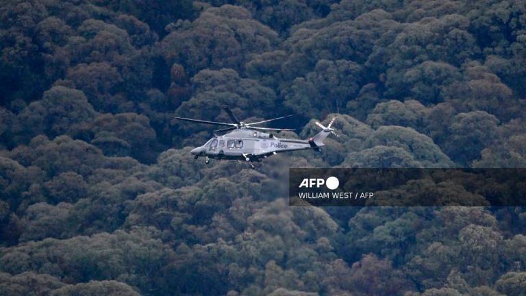A Victoria police helicopter circles the peaks as the search intensifies for a fugitive linked to the cold-blooded murder of two police officers in Porepunkah on August 27, 2025. Police searched the Australian bush on August 27, for a heavily armed 56-year-old gunman still on the run a day after allegedly killing two officers and wounding a third. - WILLIAM WEST / AFP
