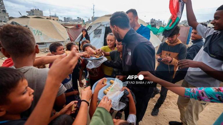 A man distributes sweets at a camp for displaced Palestinians in Nuseirat in the central Gaza Strip on October 9, 2025, following news of a new Gaza ceasefire deal. - Eyad BABA / AFP