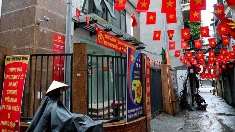 (FILES) A woman wearing a raincoat walks with her bicycle past a former local authorities’ building which closed due to Vietnam’s new administrative structure of 34 provinces and cities in Hanoi on July 1, 2025. - AFPpix