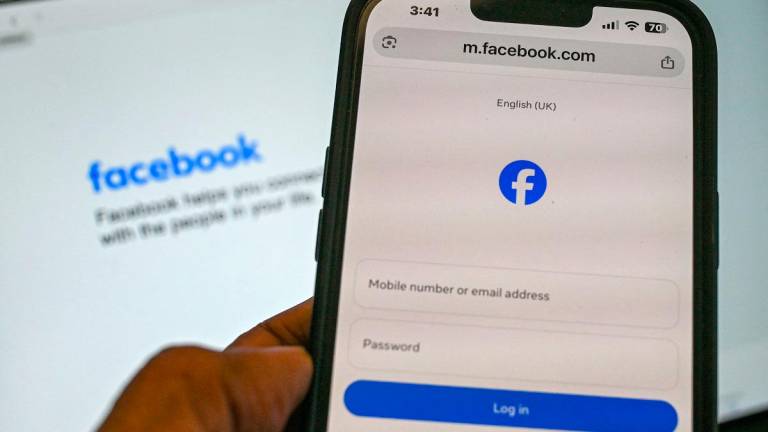 An illustration photograph taken on September 3, 2025 shows a person holding a phone on the Facebook log-in page in Singapore. - Roslan RAHMAN / AFP