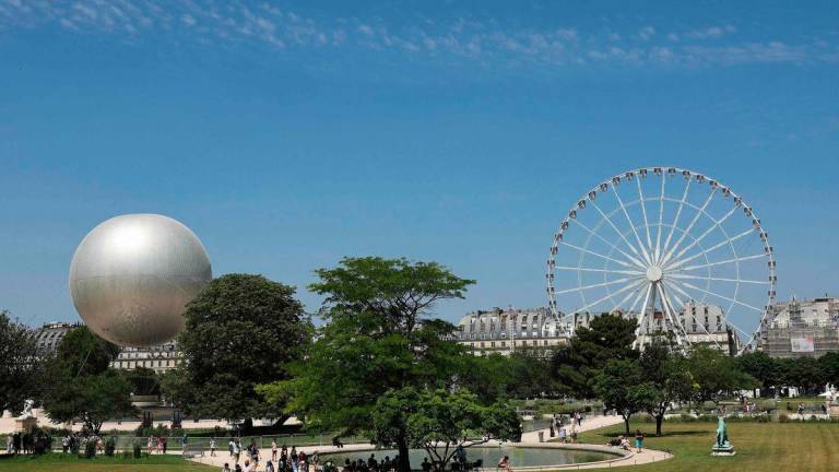 People walk pass by the Olympic Cauldron (L) and the Giant Ferris Wheel (R) at the Tuileries Garden, during a hot summer afternoon, in Paris, on June 19, 2025-AFP