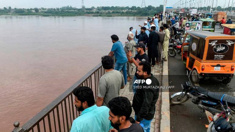 Commuters watch the Ravi River from a bridge as the government announced a flood alert in the riverside areas of Punjab province, in Lahore on August 27, 2025. - Syed Murtaza Ali / AFP