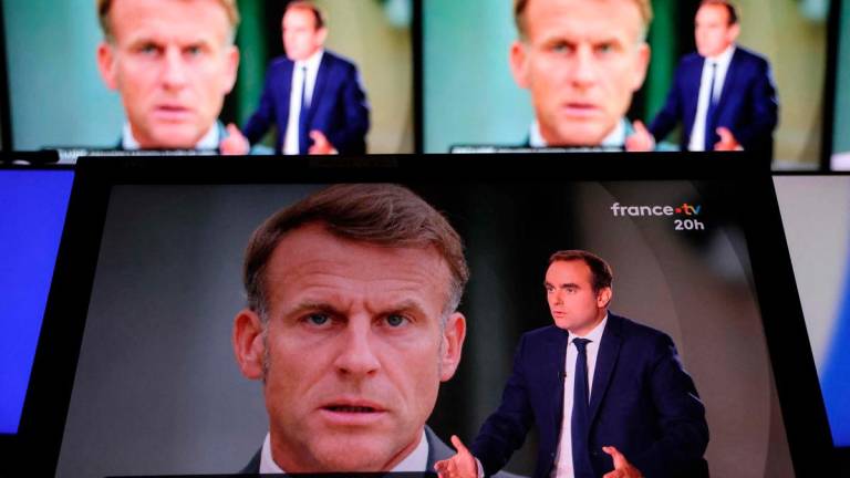 This photograph shows a television screen displaying France’s outgoing Prime Minister Sebastien Lecornu (R), with an image of France’s President Emmanuel Macron in the background, during a live broadcast interview on a set of French TV France 2 in Paris on October 8, 2025. (Photo by Ludovic MARIN / AFP)