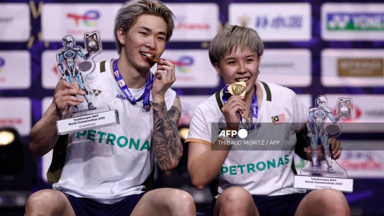 Malaysia’s Chen Tang Jie (L) and Toh Ee Wei hold their trophies as they bite their gold medals as they celebrate on the podium after beating China’s Jiang Zhen Bang and Wei Ya Xin in the mixed doubles final match at the Badminton BWF World Championships at the Adidas Arena in Paris, on August 31, 2025. - Thibaud MORITZ / AFP