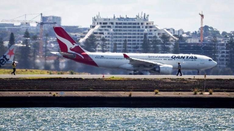 Workers check the runway as a Qantas plane prepares to take off behind them at Sydney International Airport on November 8, 2024. - AFPPIX