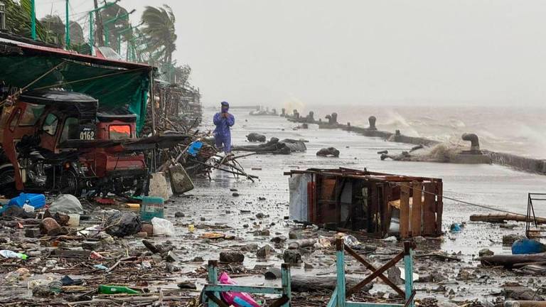 A man stands near debris on a waterfront road amid heavy rain due to weather patterns from Super Typhoon Ragasa in Aparri town, Cagayan province on September 22, 2025. Hundreds of families sheltered in schools and evacuation centres on September 22 as heavy rains and gale-force winds from Super Typhoon Ragasa lashed the northern Philippines and southern Taiwan. (Photo by John Dimain / AFP)