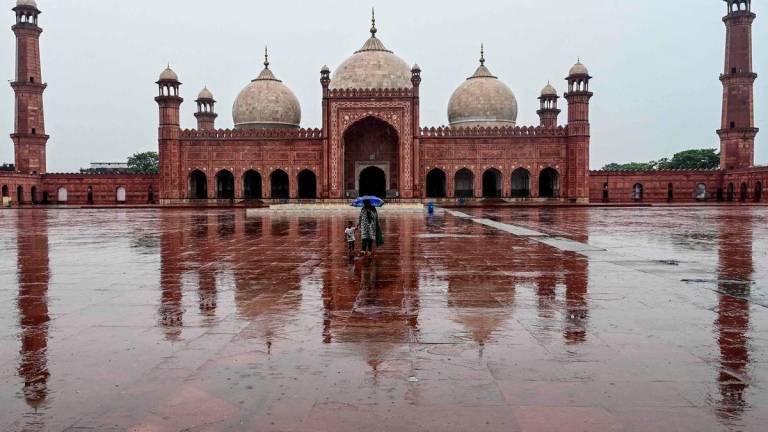 A woman holding an umbrella walks along with her child at the Badshahi Mosque as it rains in Lahore on August 14, 2025. Photo by Arif ALI / AFP