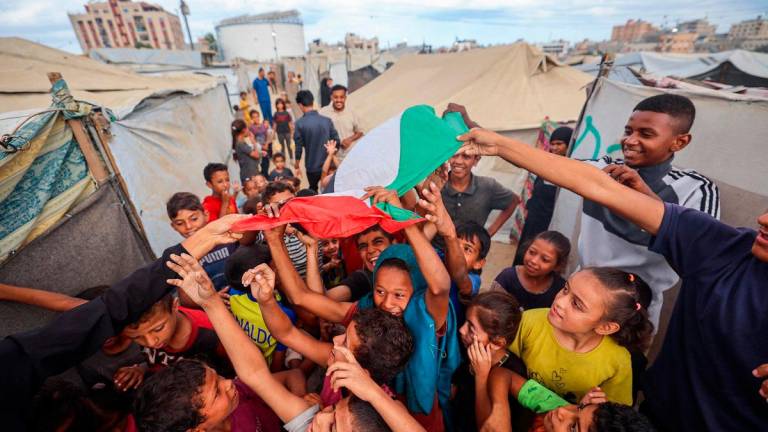 Palestinian children celebrate at a camp for displaced people in Nuseirat in the central Gaza Strip on October 9, 2025, following news of a new Gaza ceasefire deal. - Eyad BABA / AFP