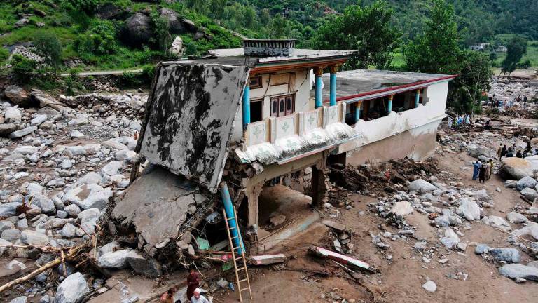 An aerial view shows flood survivors standing near a damaged house surrounded by heavy rocks in the Buner district of mountainous Khyber Pakhtunkhwa province on August 17, 2025. - Abdul MAJEED / AFP