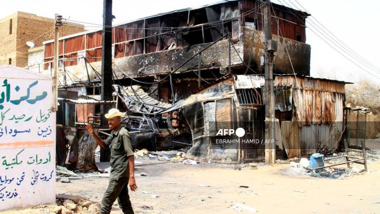 A Sudanese army soldier waves as he walks past a war-damaged building in Salha, south of Omdurman, two days after the Sudanese army recaptured it from the paramilitary Rapid Support Forces (RSF), on May 22, 2025. - Ebrahim Hamid / AFP