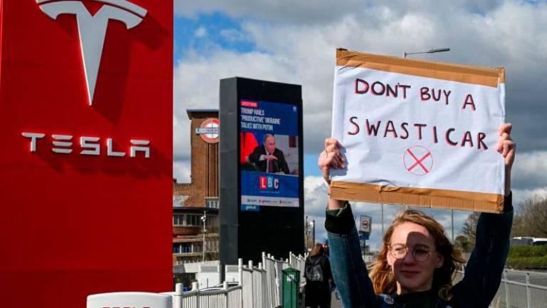 A demonstrator holds an anti-Tesla poster during a protest encouraging people to boycott Tesla in opposition to Tesla CEO Elon Musk’s political involvement in the U.S. government, outside the Tesla Centre Park Royal in London, Britain, REUTERSpix