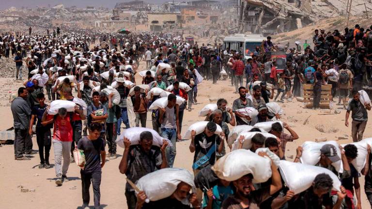 People walk with sacks of flour delivered after trucks carrying humanitarian aid entered northern Gaza on July 27, 2025 coming from the Zikim border crossing. - BASHAR TALEB / AFP