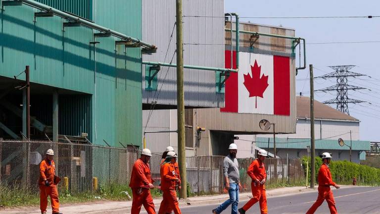 A Canadian national flag is seen in the background as workers cross the street in front of ArcelorMittal Dofasco’s steel manufacturing buildings in Hamilton, Ontario, Canada, on Wednesday, June 4, 2025. AFP