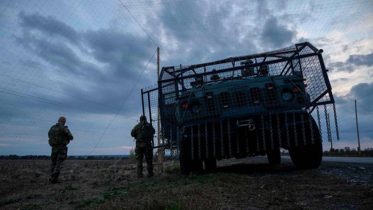 Ukrainian soldiers stand before an armoured military vehicle surrounded by a cage to protect against drone attacks on a road near Oleksandrivka, on October 6, 2025 amid the Russian invasion of Ukraine. - Ed JONES / AFP