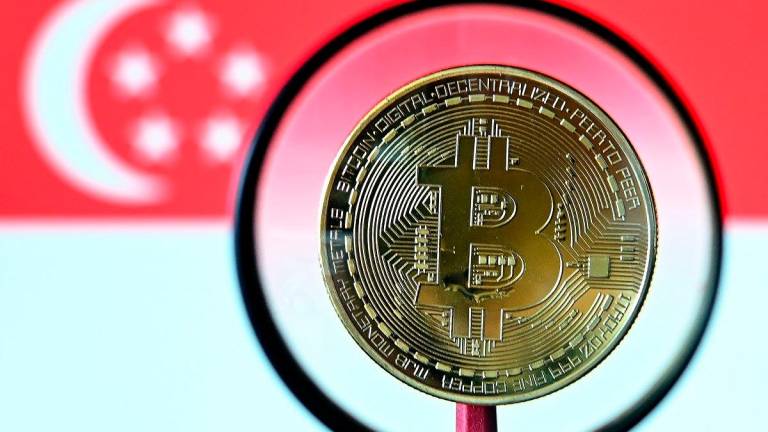 This illustration photograph taken on June 30, 2025 shows a Bitcoin cryptocurrency representation coin seen through a microscope against the backdrop of the Singapore national flag, in Bangkok. - AFPpix