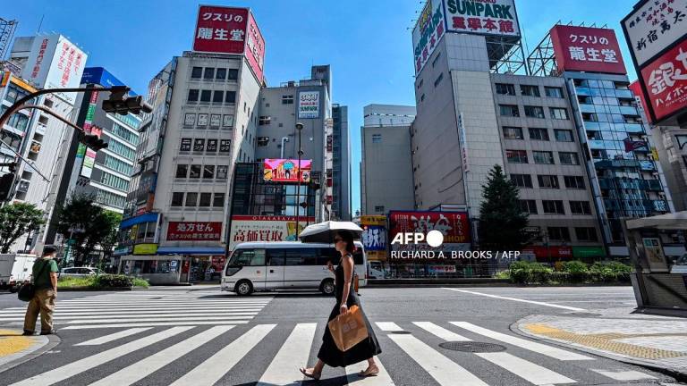 A woman (C) carries an umbrella to shelter from the sun as pedestrians cross a street in the Kabukicho entertainment area of Shinjuku in central Tokyo on July 29, 2025. - Richard A. Brooks / AFP