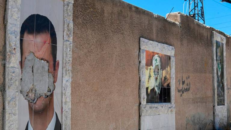 Defaced portraits of Syria’s ousted president Bashar al-Assad (L) and his late father Hafez al-Assad (C) hang on a wall in the capital Damascus on June 2, 2025. (Photo by LOUAI BESHARA / AFP)