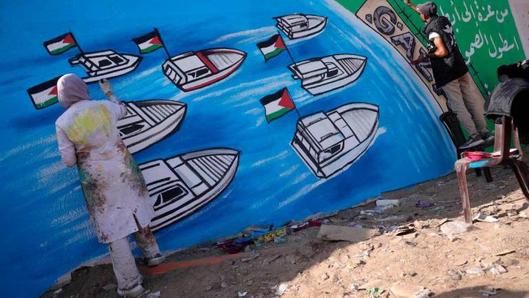 Palestinian artists work on a mural painting representing the Global Sumud Flotilla bound for Gaza, as a gift of appreciation for the activists who were aboard, in Deir el-Balah in the central Gaza Strip on October 3, 2025. (Photo by Bashar TALEB / AFP)