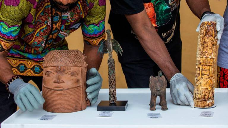 National Museum exhibition officers adjust the Head of a the king Oba of Benin (L), the Bird of Prophecy (2nd L), the Statue of a Leopard (2nd R), and the Carved Elephant Tusk (R), all returned artefacts from the “Benin Bronzes” collection at the signing ceremony and handover of the 119 Benin bronzes returned from the Netherlands to Nigeria at the National museum Onikan in Lagos on June 21, 2025. - TOYIN ADEDOKUN / AFP