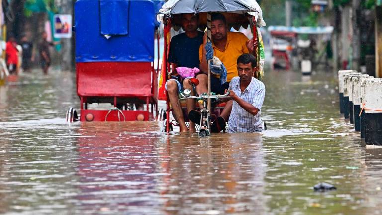 Local residents commute on a cycle rickshaw through a flooded street after heavy monsoon rains in Guwahati on August 13, 2025. Deadly floods and landslides are common during the monsoon season from June to September, but experts say climate change, coupled with urbanisation, is increasing their frequency and severity. - Biju BORO / AFP