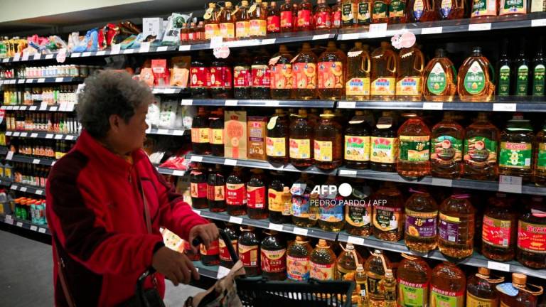 A shopper browses past shelves of cooking oil for sale at a supermarket in Beijing on October 15, 2025. - AFPPIX
