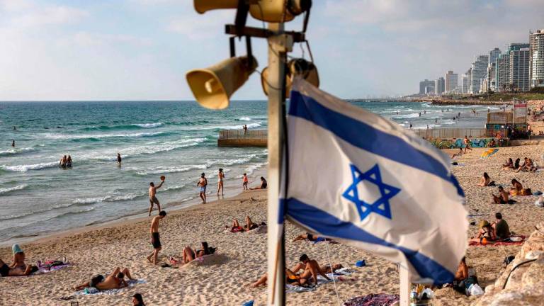 An Israeli flag flies beneath siren loudspeakers as people gather by the surf at a beach in Tel Aviv on June 21, 2025. (Photo by AHMAD GHARABLI / AFP)