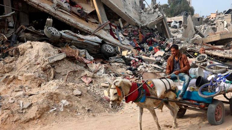 A Palestinian man rides a horse-pulled cart, next to a destroyed building where personal belongings of people and a car are sandwiched between the layers of its rubble, in Gaza City on November 2, 2024, amid the ongoing war between Israel and Hamas militants. (Photo by Omar AL-QATTAA / AFP)