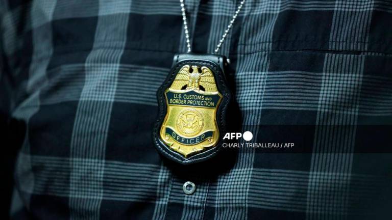 A federal agent’s badge hangs from his neck as he waits outside a courtroom at New York Federal Plaza Immigration Court in the Jacob K. Javits Federal Building, New York City, August 20, 2025. US President Donald Trump has made deporting undocumented immigrants a key priority for his second term, after successfully campaigning against an alleged “invasion” by criminals. (Photo by CHARLY TRIBALLEAU / AFP)