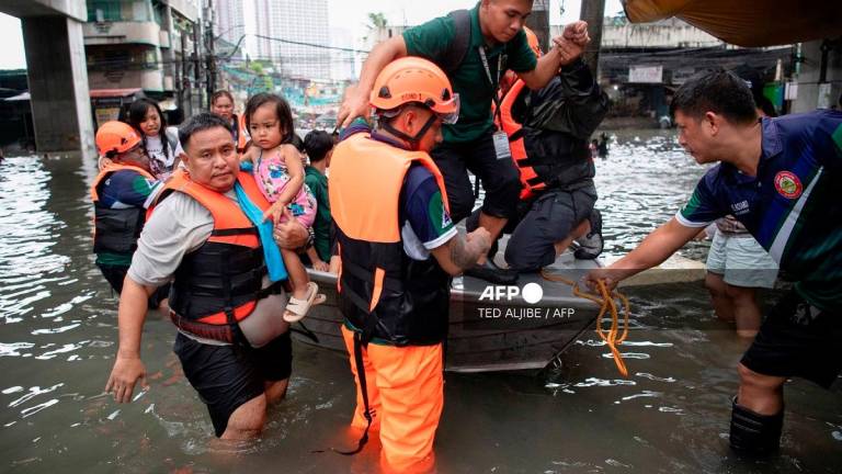 Rescuers use a boat to evacuate stranded people through a flooded street in Manila on July 21, 2025, after Typhoon Wipha brought heavy rains and flooding to the Philippines, where two people have been reported missing, according to the country's National Disaster Risk Reduction and Management Council. - Ted ALJIBE / AFP