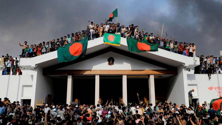 Anti-government protestors display Bangladesh’s national flag as they storm Prime Minister Sheikh Hasina’s palace in Dhaka on August 5, 2024. - AFPPIX