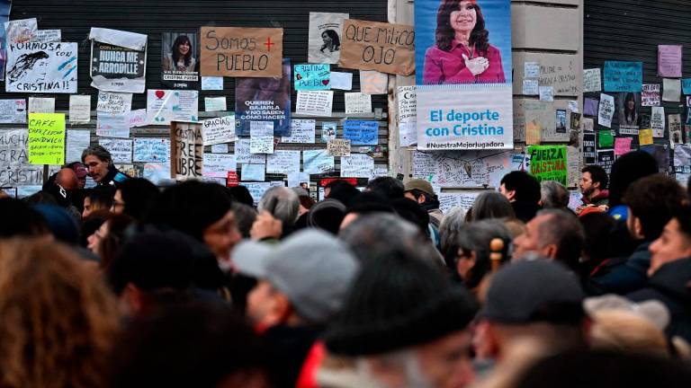 People gather past a wall with messages in support of former Argentine President Cristina Fernandez de Kirchner outside her residence in Buenos Aires on June 17, 2025. On June 17, 2025, a judge agreed to let Argentine ex-president Cristina Kirchner to serve a six-year fraud sentence at home, easing concern among backers keeping a vigil outside her apartment with plans to protest in case she was jailed. - Luis ROBAYO / AFP