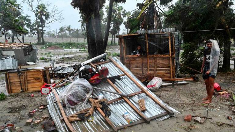 People stand next to a damaged shop following the landfall of Cyclone Remal near a beach in Kuakata on May 27, 2024. Residents of low-lying coastal areas of Bangladesh and India surveyed the damage on May 27 as an intense cyclone weakened into heavy storm, with at least two people dead, roofs ripped off and trees uprooted. (Photo by MUNIR UZ ZAMAN / AFP)