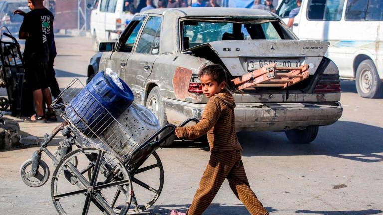 For visual purposes only: A girl pushes a broken wheelchair loaded with jerrycans along a road at a camp for people displaced by war in northern Nuseirat in the central Gaza Strip on October 7, 2025. (Photo by BASHAR TALEB / AFP)