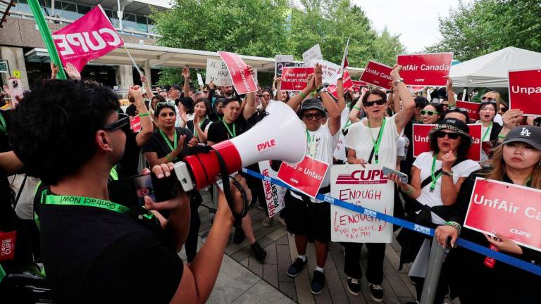 CUPE president Mark Hancock appears on a mobile phone screen as striking Air Canada flight attendants listen to a remote broadcast by megaphone by Hancock on the current situation, as they defy a back to work order at Vancouver International Airport in Richmond, British Columbia, Canada August 18, 2025. - REUTERSPIX