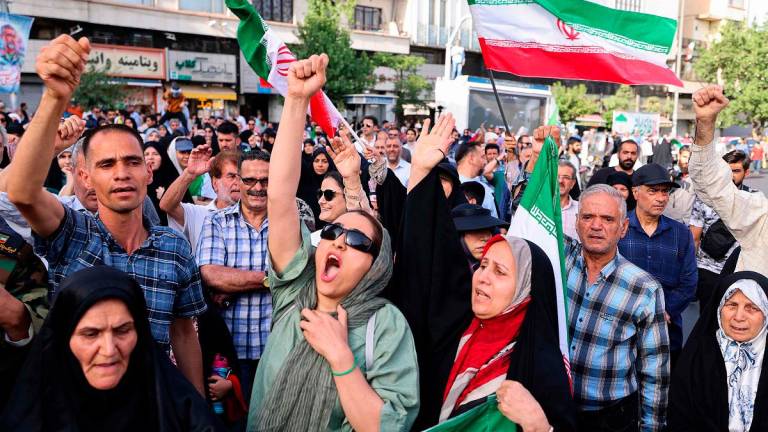 Iranians lift flags and chant during a rally protesting the US attack on Iran in Enghelab Square in Tehran on June 22, 2025. Iran’s President Masoud Pezeshkian condemned US strikes on nuclear sites on June 22, saying in his first response that the attack revealed Washington was “behind” Israel’s military campaign in the Islamic republic. - ATTA KENARE / AFP