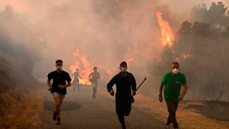 People run by a burnt area during a wildfire near the village of Larouco, in the province of Ourense, in northwestern Spain on August 13, 2025- AFP