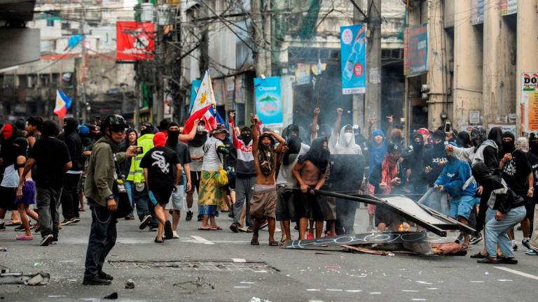 Smoke rises from burning objects as demonstrators show their middle fingers and shout towards police officers during a protest denouncing what they say is corruption linked to flood control projects, in Manila, Philippines, September 21, 2025. REUTERS/Lisa Marie David