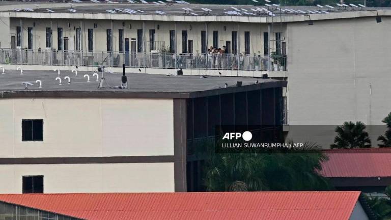 (FILES) This photo taken on September 17, 2025 shows people on a balcony of a building with what appears to be Starlink satellite dishes on the roof in the KK Park complex in Myanmar’s eastern Myawaddy township, as pictured from Mae Sot district in Thailand’s border province of Tak. - Lillian SUWANRUMPHA / AFP