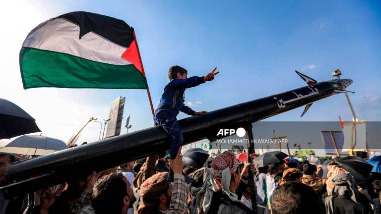 A boy sitting on a missile bearing the name Palestine gestures while next to him a man waves a Palestinian flag, during a rally by supporters of Yemen's Huthis condemning Israel and in support of Palestinians, near the Saleh Grand Mosque in the Huthi-held capital Sanaa on October 3, 2025. - AFP