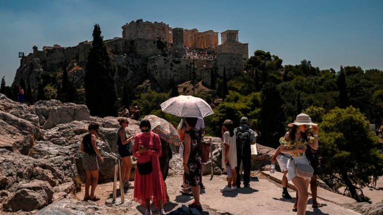 Tourists some holding umbrellas, gather opposite Acropolis Hill in Athens on July 8, 2025. (Photo by Aris MESSINIS / AFP)