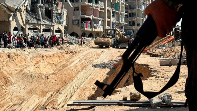 Hamas militant stands guard, as heavy machinery operates at the site where searches are underway for the bodies of hostages killed after being seized by Hamas during the October 7, 2023 attack, amid a ceasefire between Israel and Hamas, in Khan Younis, southern Gaza Strip, October 17, 2025. - REUTERSPIX