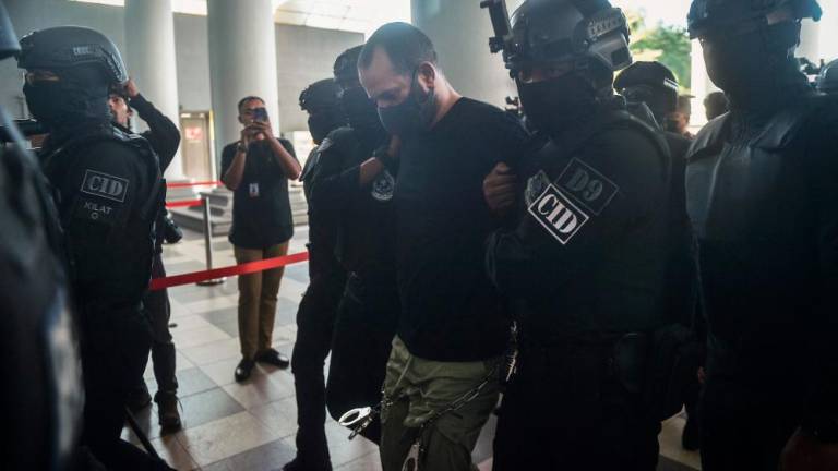 An Israeli man identified as Shalom Avitan (C) is escorted by Malaysian police upon his arrival at a court to face charges of possessing six handguns and 200 bullets in Kuala Lumpur on April 12, 2024. (Photo by Arif Kartono / AFP)