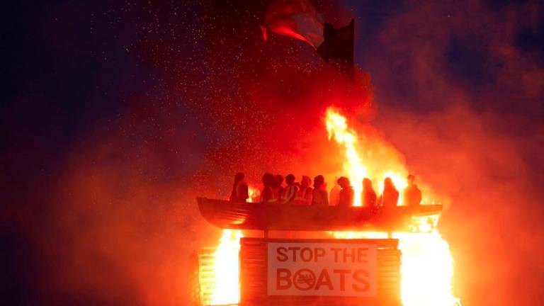 A loyalist bonfire burns after being set alight, featuring a model effigy of a boat containing mannequins portrayed as migrants in lifejackets, with a sign reading Stop the Boats, during annual bonfire events marking the 1690 Battle of the Boyne, in Moygashel, Northern Ireland, July 10, 2025. - REUTERSPIX