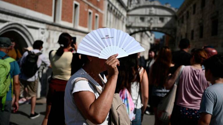 A woman protects herself from the sun with a hand fan near the Bridge of Sighs, on a hot summer day in Venice on June 28, 2025. - AFPPIX