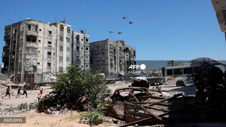 Palestinian run towards aid pallets as they parachute down after being dropped from a military plane near Jabalia in the northern Gaza Strip on August 20, 2025. - AFP