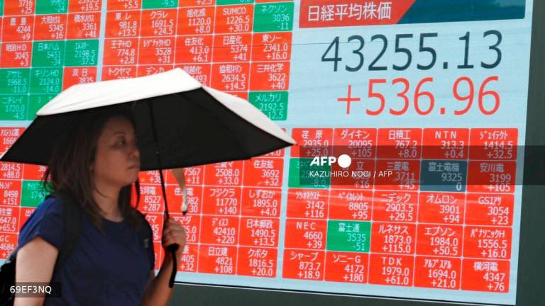 A woman walks in front of an electronic quotation board displaying the Nikkei Stock Average on the Tokyo Stock Exchange in Tokyo on August 13, 2025. (Photo by Kazuhiro NOGI / AFP)