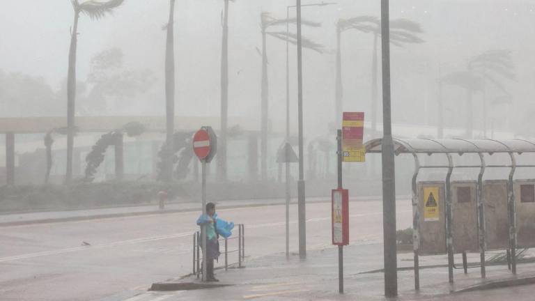 A woman clings to a traffic sign to maintain balance against strong winds from Super Typhoon Ragasa in Hong Kong, China, September 24, 2025. - REUTERSPIX